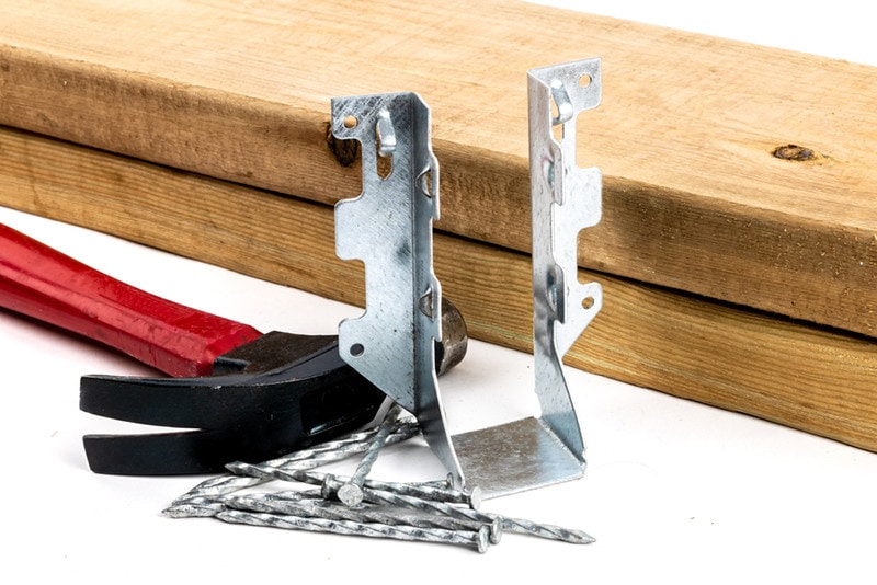 A galvanized steel joist hanger with hammer and nails as be used n residential construction