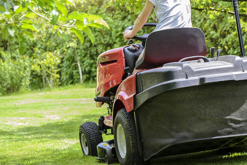 cropped person mowing the grass with ride-on mower