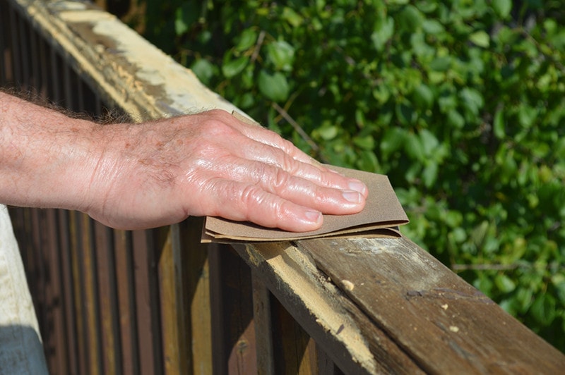 Hand With Sandpaper Sanding the Deck Railing