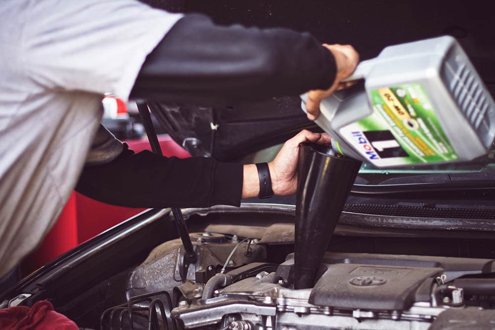 man refilling fluid on car engine_TimMossholder_Unsplash