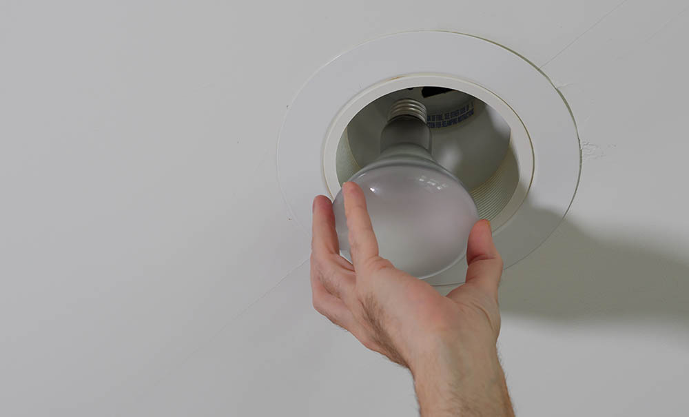 person replacing bulb on can recessed lighting