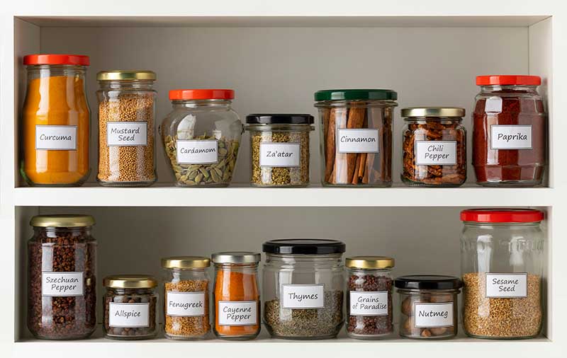 Recycled glass jars with a variety of dried herbs in a row on the kitchen shelf