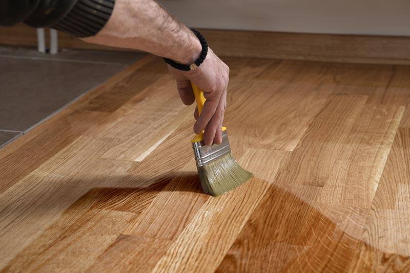 Varnishing lacquering parquet floor by paintbrush - second layer