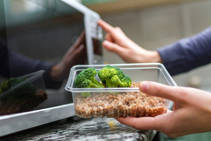 woman going to heat up a plastic container with food in the microwave