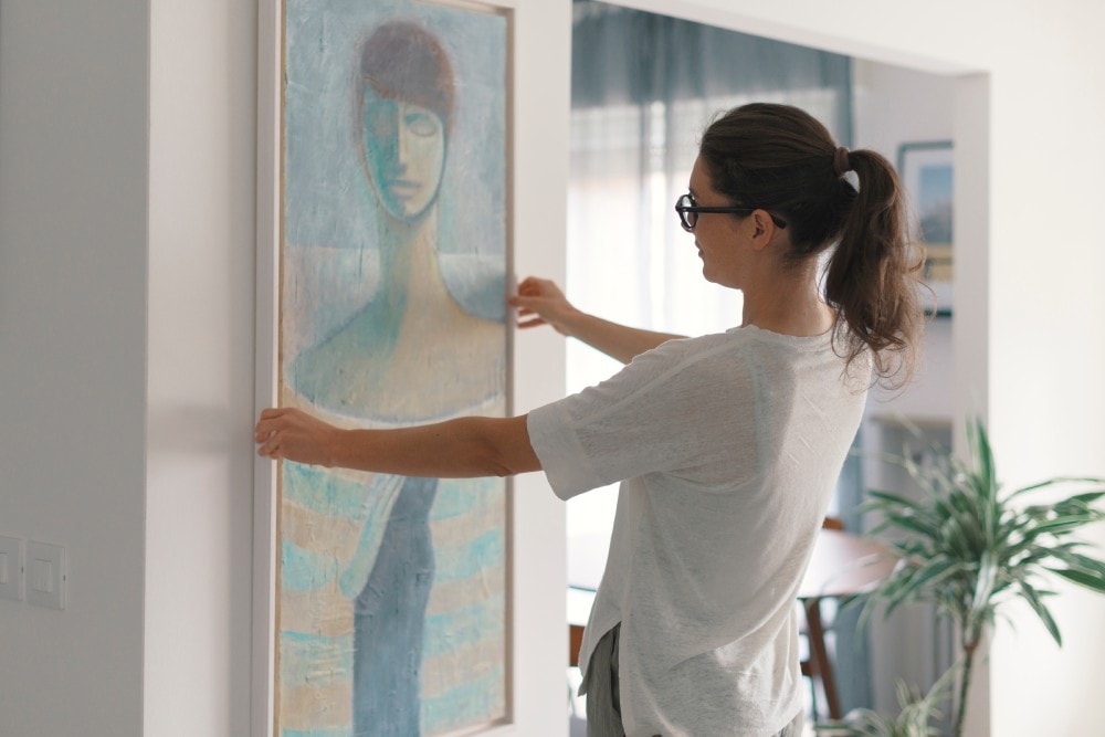 Woman hanging a painting at home and decorating her contemporary living room