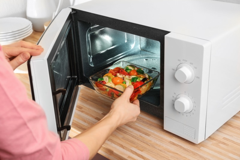 woman putting glass bowl with vegetable in the microwave