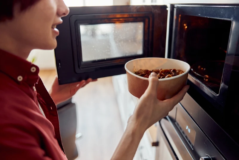 man placing food in a cardboard container into the microwave