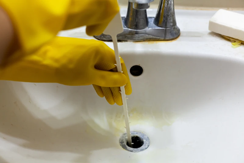person using a drain snake to remove hair from clogged sink drain
